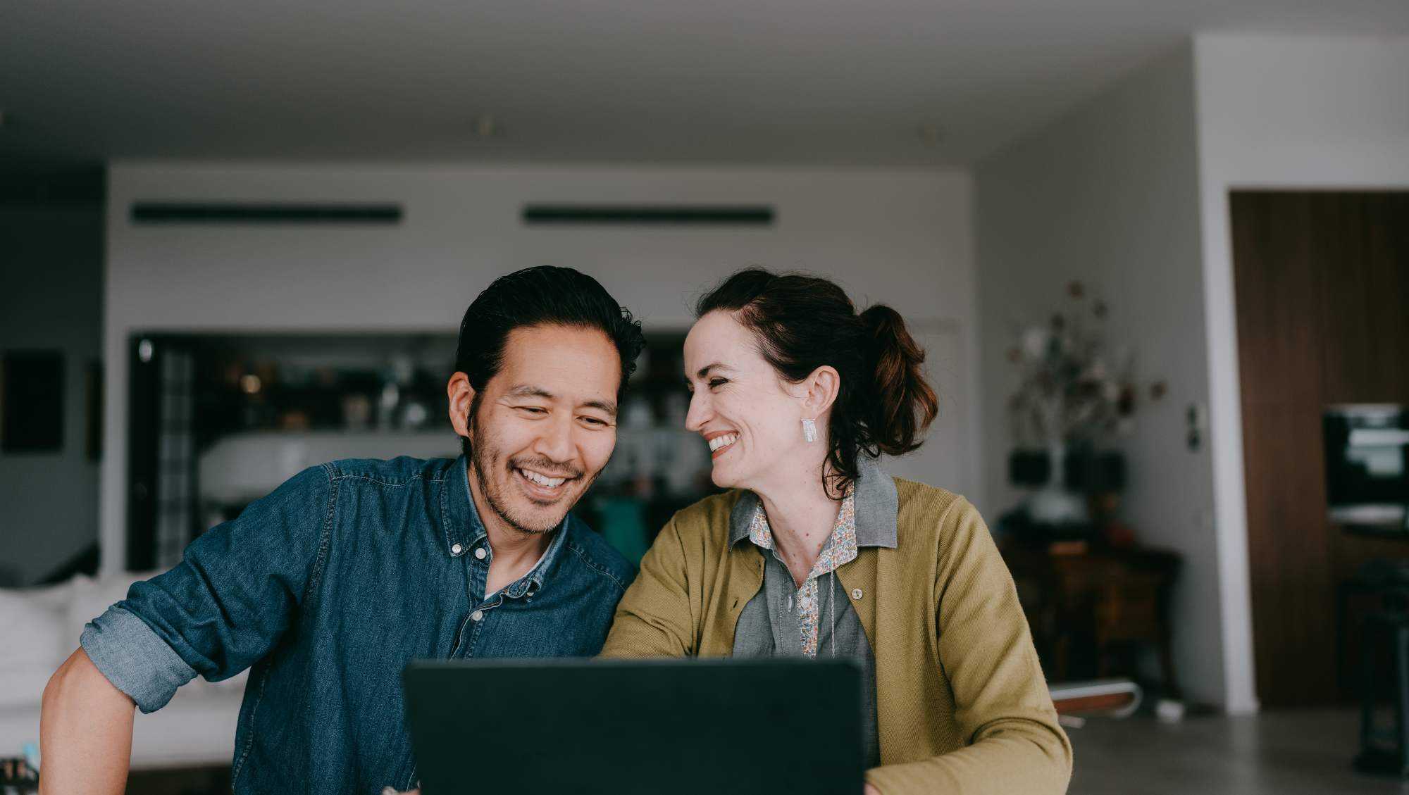 a couple on a laptop smiles as they calculate their trip cost for travel insurance