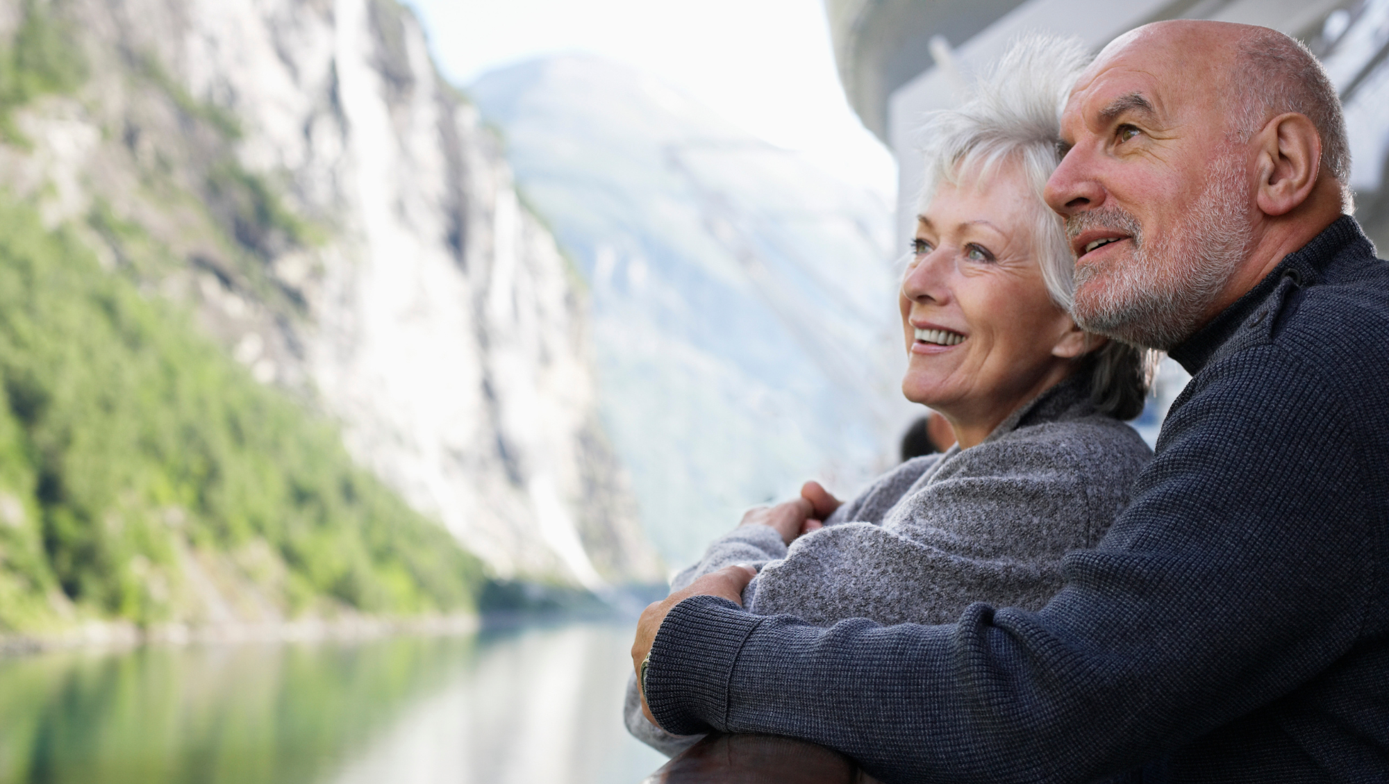 an older couple embraces on a cruise ship balcony, taking in views after reading a cruise safety guide