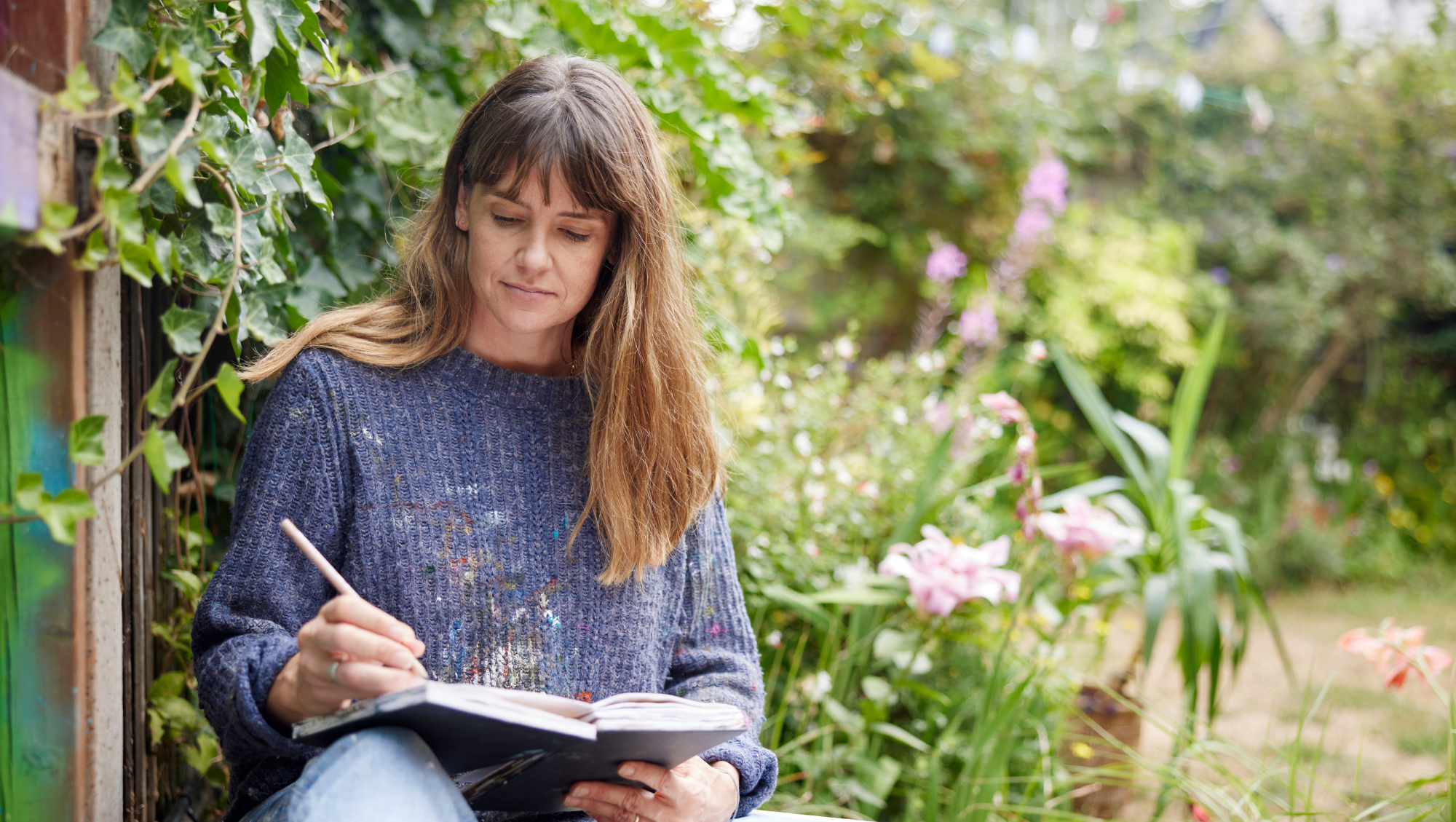 a woman sits in a garden with a notepad, going over her travel insurance checklist