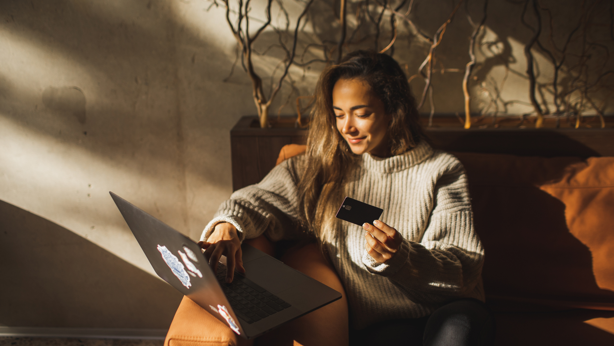 a young woman on her laptop and holding a credit card while wondering, "How much is travel insurance?"