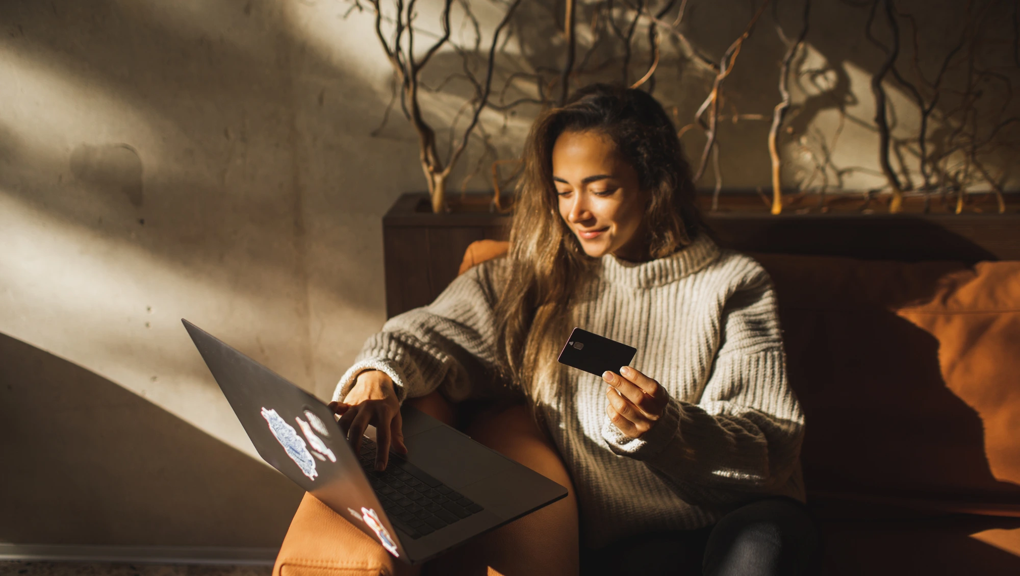 a woman sits on a couch with natural light, holding her credit hard and looking up "How much is travel insurance?"