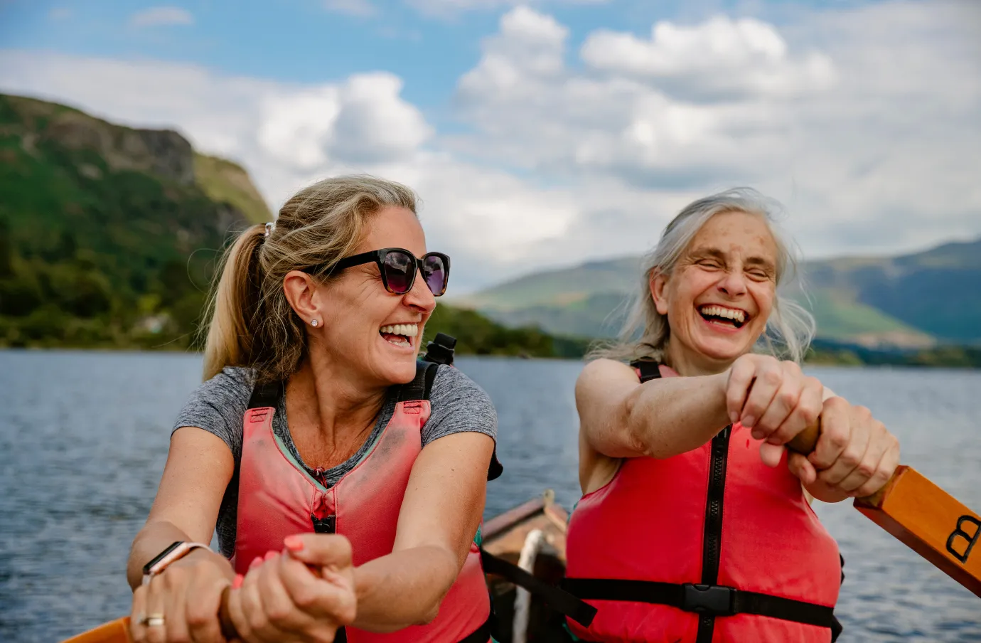 two women with travel insurance for the UK row on a scenic lake in England's Lake District National Park