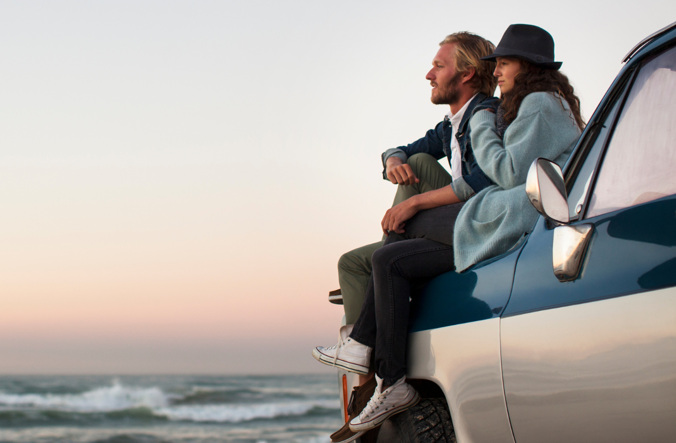 a man and woman with travel insurance for couples sit on a van by the ocean and watch the sunset