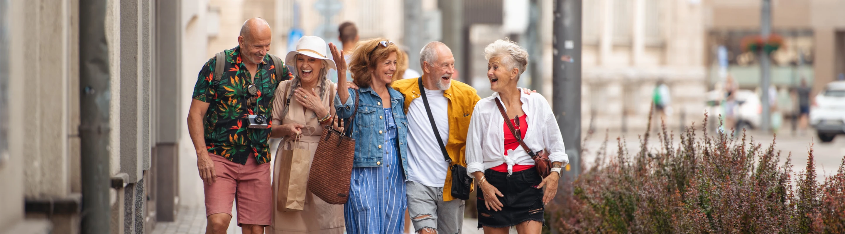 six older adults with group travel insurance laugh and chat as they walk down a city street on vacation