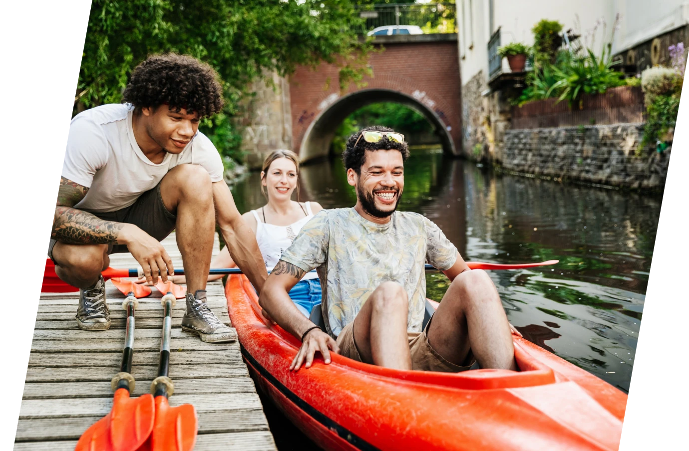 A young man pushes a red kayak away from the dock so his two friends with group travel insurance can paddle through the canal