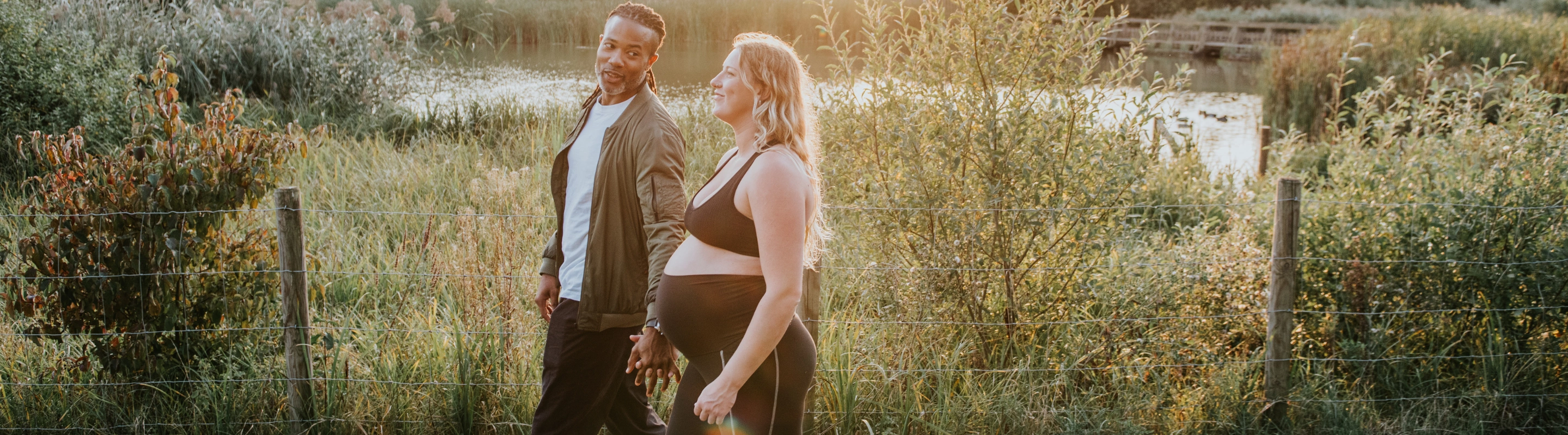 a pregnant, mixed-race couple with travel insurance for pregnancy walks through a green park at sunset