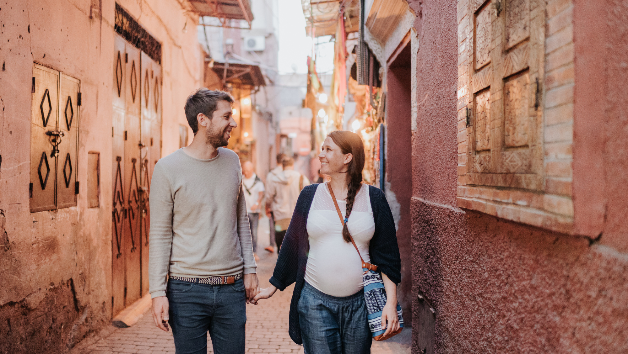 a pregnant couple holds hands as they walk through a historic town on vacation, beating travel anxiety 