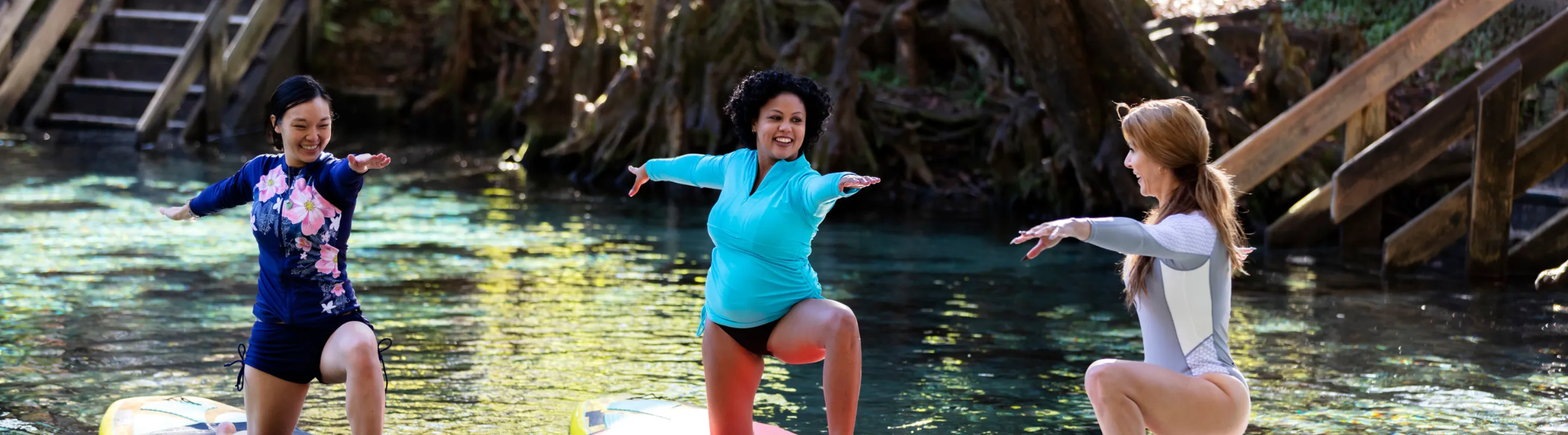 Three women with travel insurance for Florida doing yoga on paddleboards in a natural spring