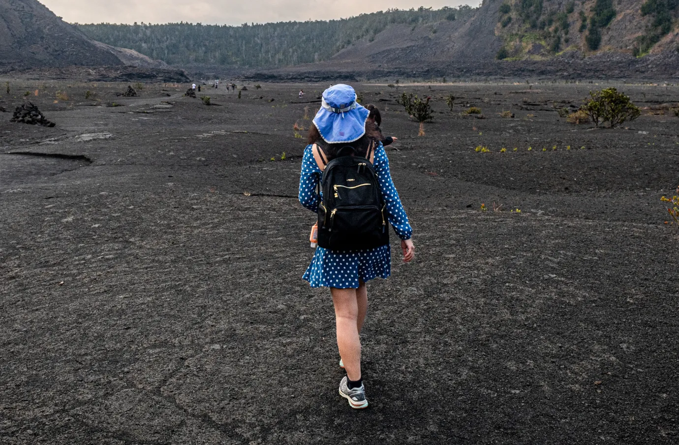 a woman in blue hikes a volcanic landscape, insured with volcano travel insurance