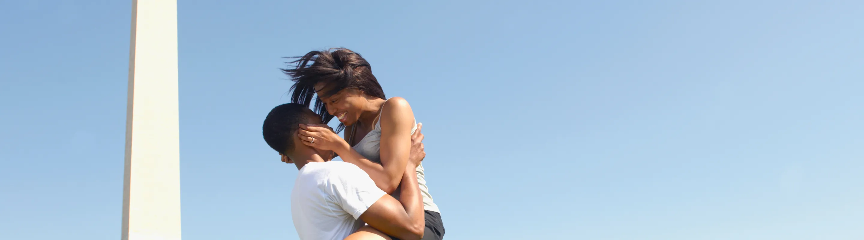 a couple with travel insurance for Washington, D.C. stands on the National Mall with the Washington Monument nearby