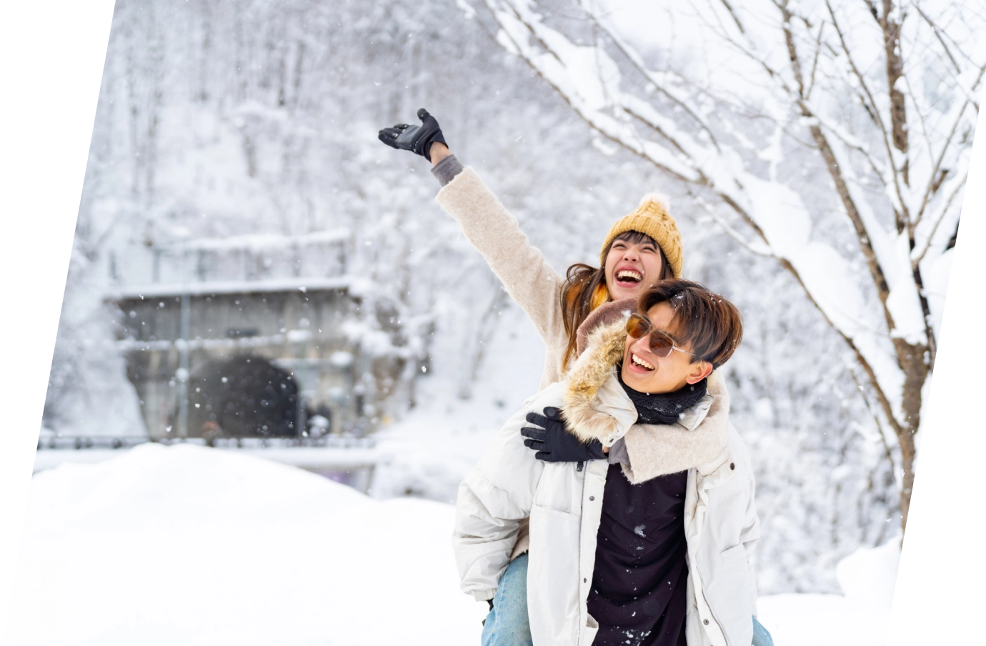 a woman with ski insurance piggyback rides on her partners back during snowfall in a park setting