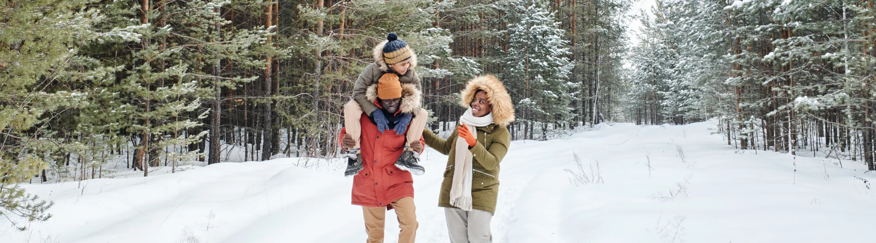 two young, mixed-race parents and their child walk through a snowy forest on a winter trip after researching ski insurance